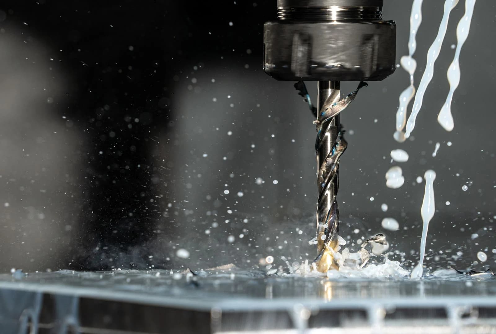 CNC drill cutting into an aluminium workpiece with coolant spraying, chips flying off the flutes