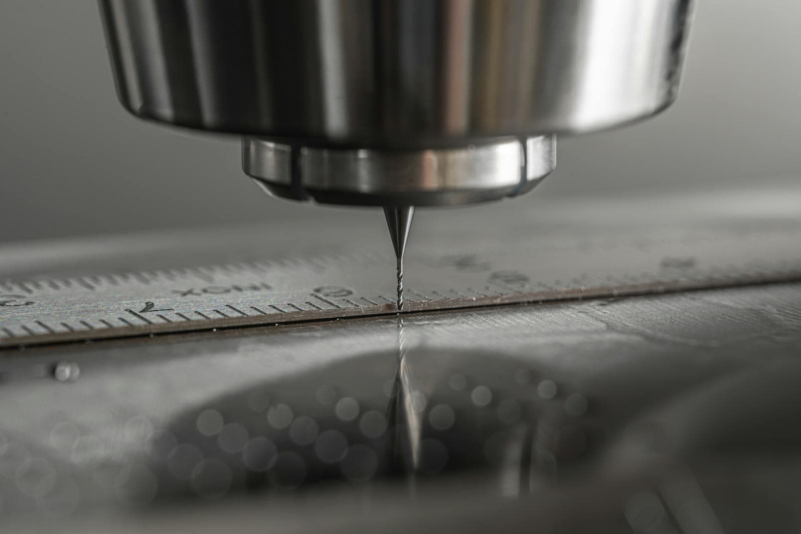 Macro close-up of a CNC milling machine end mill above a steel rule on a machined surface