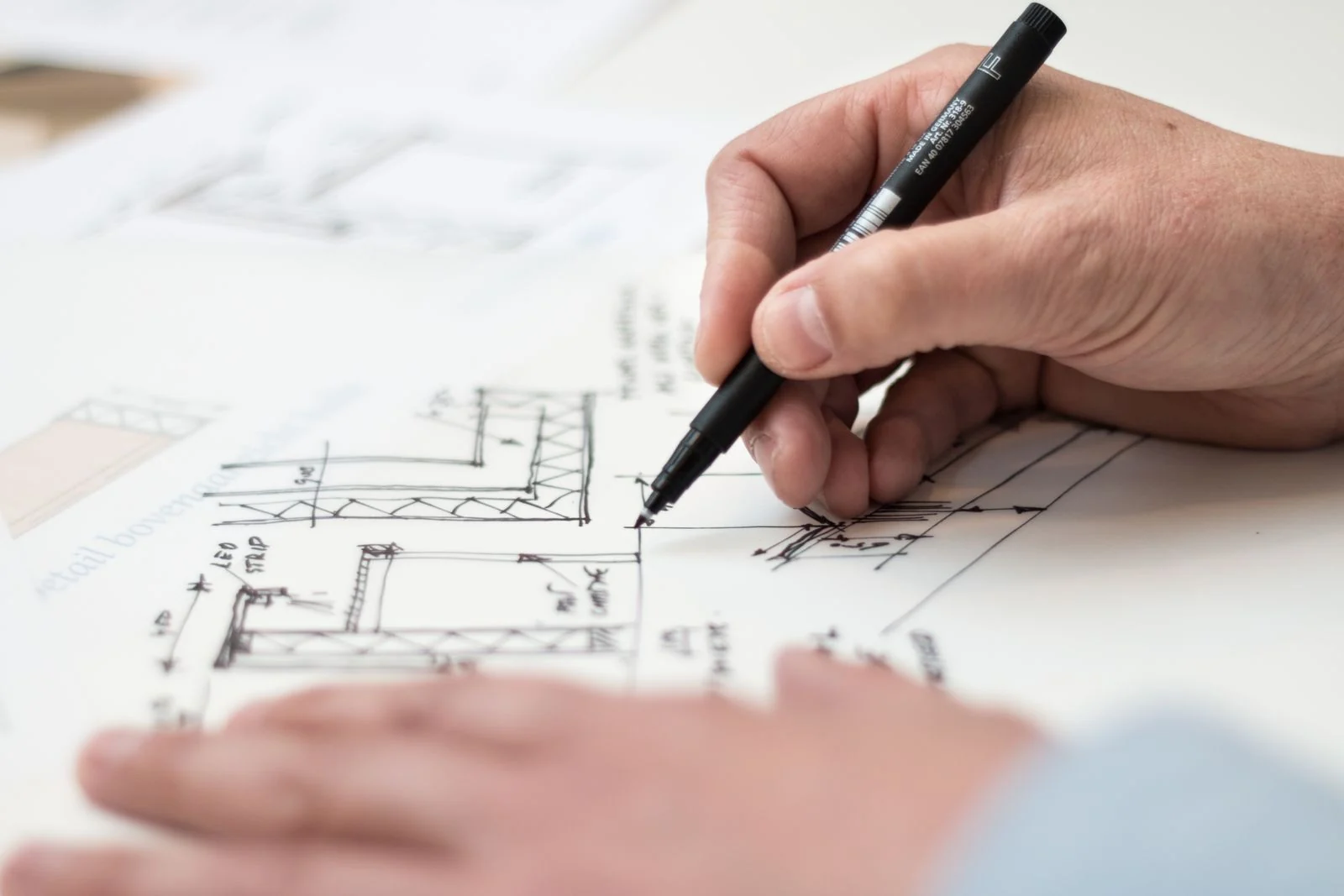 Engineer's hand drafting a dimensioned construction detail on a technical drawing with a fineliner pen