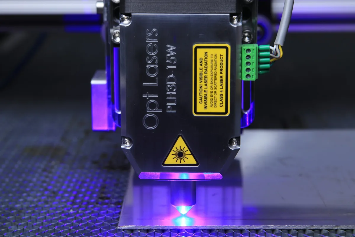 A compact laser head with a focused beam, the kind of diode or CO2 laser that engraves a vector logo onto wood or acrylic