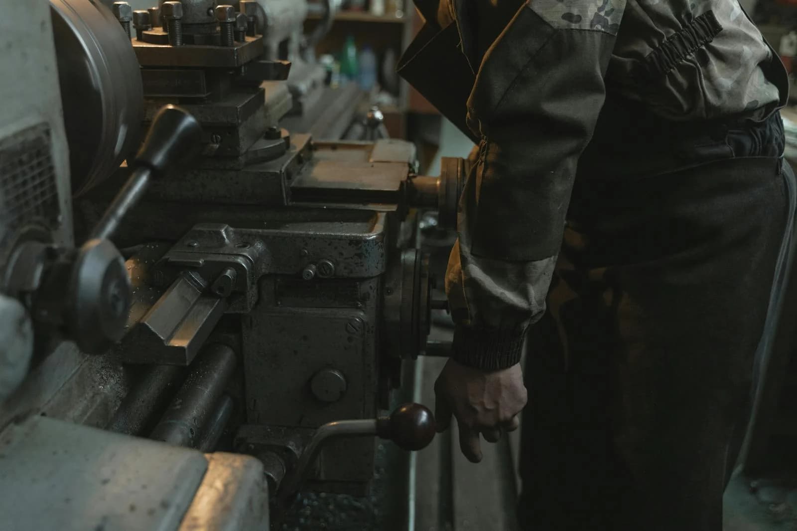 Machinist operating a manual lathe in a workshop, hand on the carriage handwheel