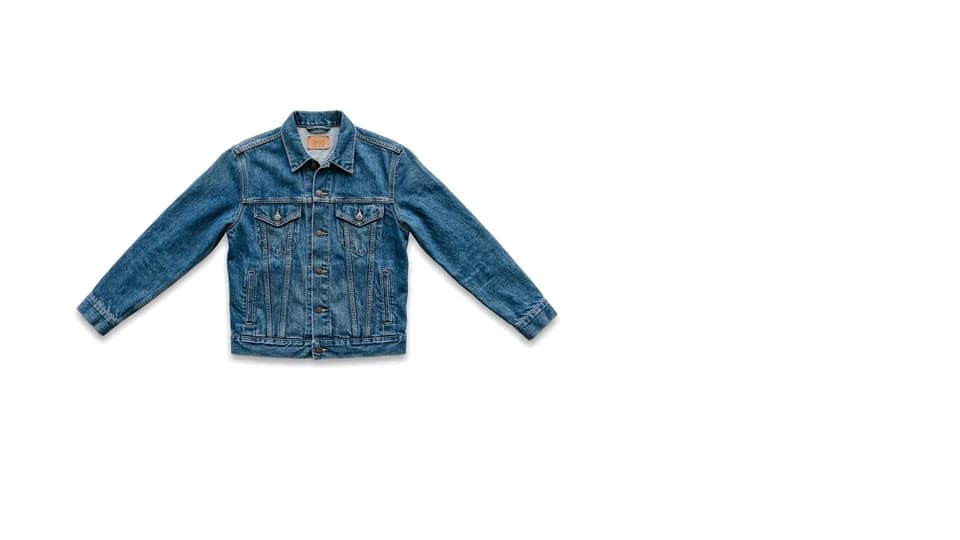 A denim trucker jacket laid flat, photographed on white